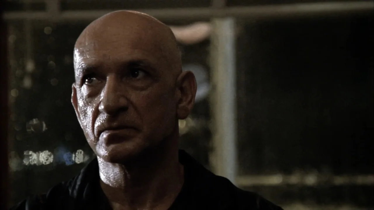 Suspect Zero (2004) movie still: closeup — A dimly lit room with a dark, indistinct background visible through a window. An older man with damp skin…
