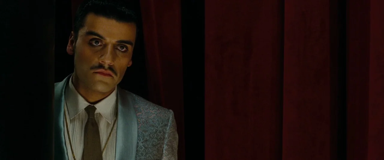 Sucker Punch (2011) movie still: medium — A dark space features heavy red velvet curtains draped in the background. A man stands partially obscured…