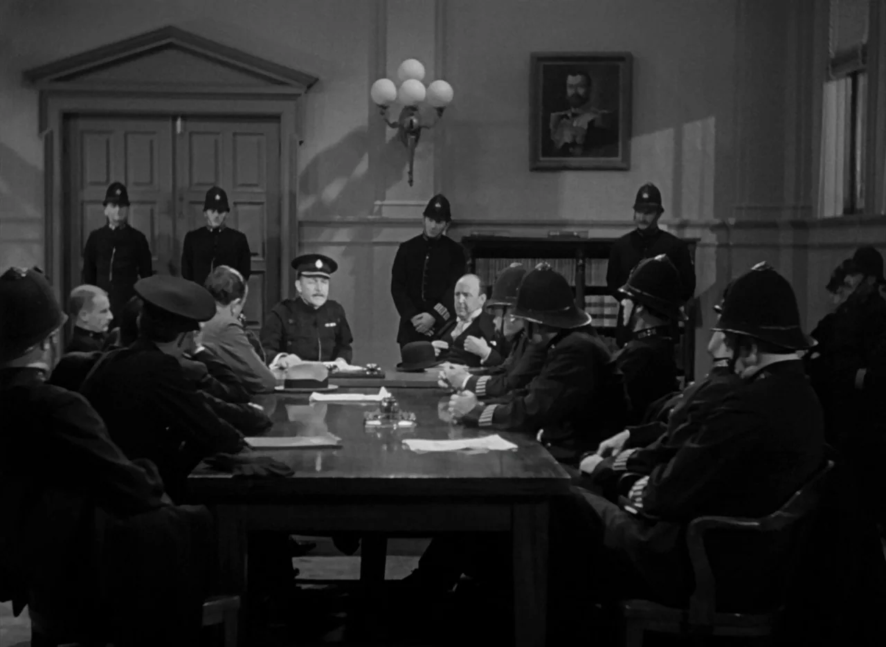 The Invisible Man (1933) (1933) movie still: wide — A group of police officers gather around a large wooden table in an office. A portrait hangs on…