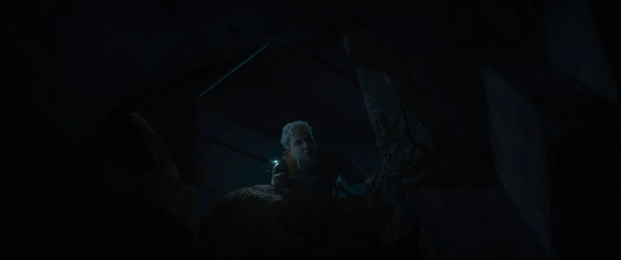 Evil Dead Rise (2023) movie still: medium — A dark, cramped space features jagged concrete walls surrounding a central opening. A young man stares…