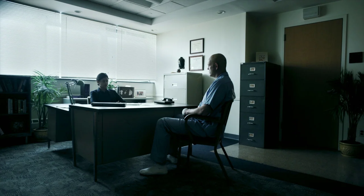 Brawl in Cell Block 99 (2017) movie still: wide — A stark room with grey carpet, a metal desk, and a tall filing cabinet. A man in hospital scrubs…