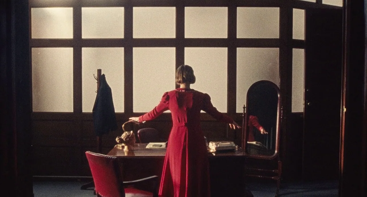 Chained For Life (2018) movie still: fullbody — A vintage room features a large window wall partitioned into rectangular glass panes. A woman in a…