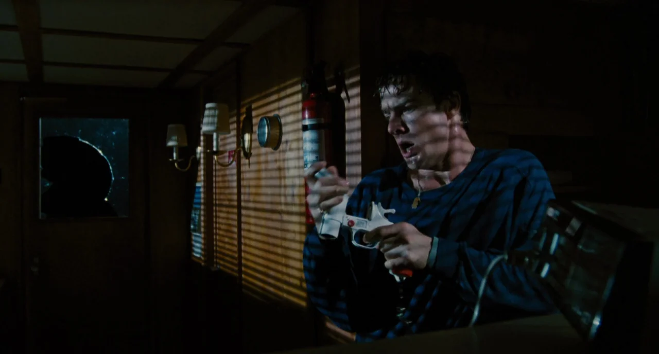 The Big Easy (1986) movie still: medium — A dimly lit room features wood-paneled walls and a window covered by horizontal blinds. A man with wet…