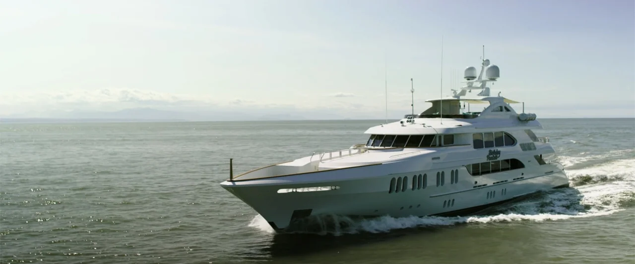 Overboard (2018) movie still: wide — A large white luxury yacht cruises across a vast expanse of calm open water. The vessel moves from left to…