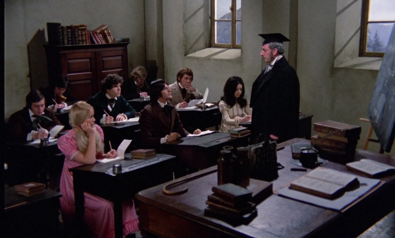 The Horror of Frankenstein (1970) movie still: wide — A 19th-century academic classroom with wooden desks and a large instructor's table. Students…