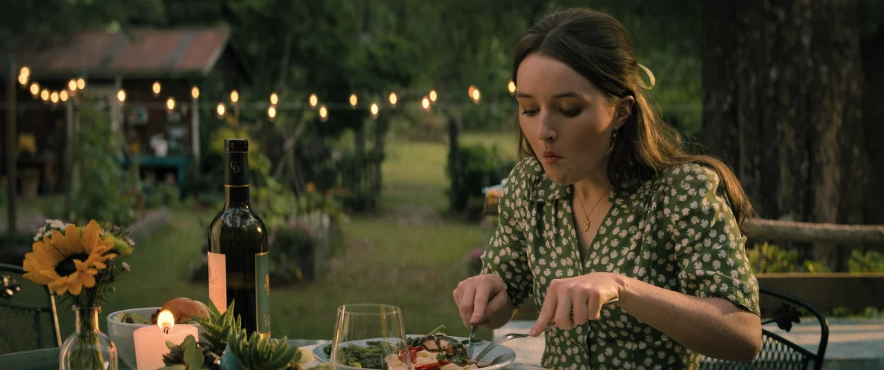 No One Will Save You (2023) movie still: medium — A backyard dining area features a table set with food and string lights. A woman eats a meal at…