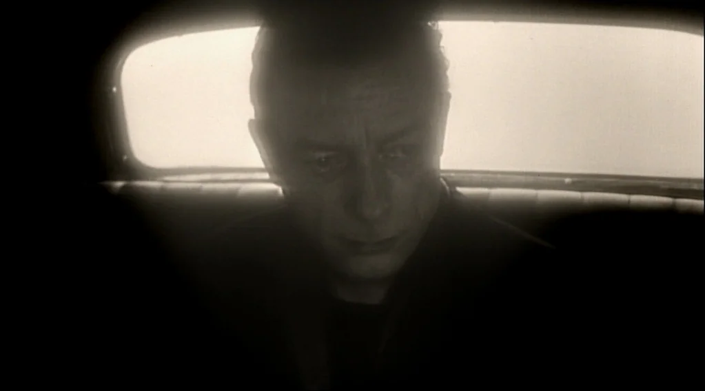 Wings Of Desire (1987) movie still: closeup — The interior of a moving car features a man seated against a bright window. The subject faces forward…