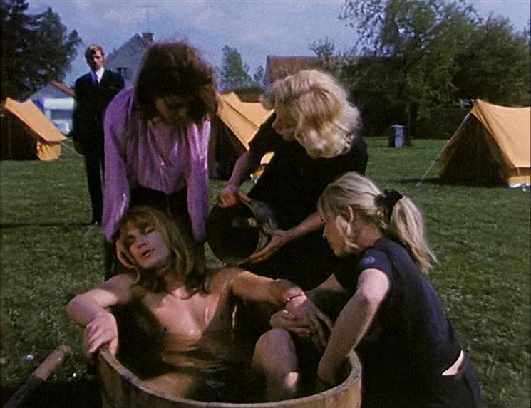 The Niklashausen Journey (1970) movie still: medium — A group of people gathers in a grassy meadow with canvas tents in the background. Three women…