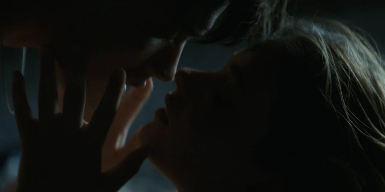 My Fault (2023) movie still: closeup — A dimly lit interior space with two people in close proximity to each other. One person reaches out to touch…