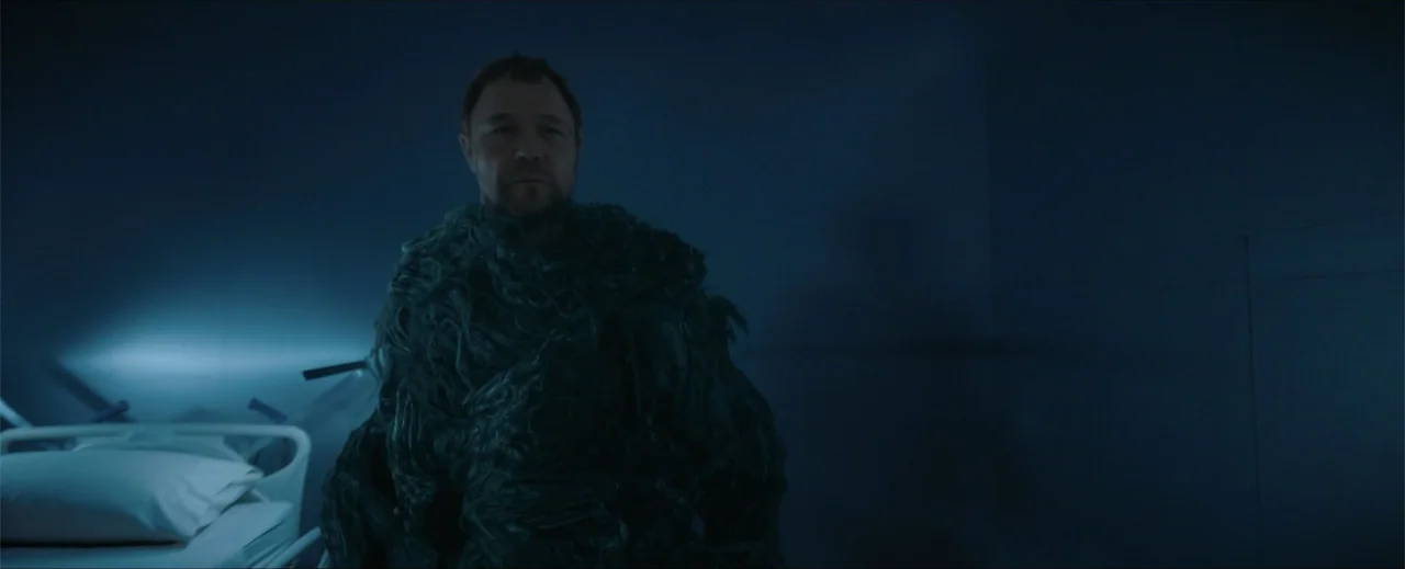 Venom: The Last Dance (2024) movie still: medium — A dimly lit hospital room features a bare bed frame with white pillows. A man covered in a dark,…