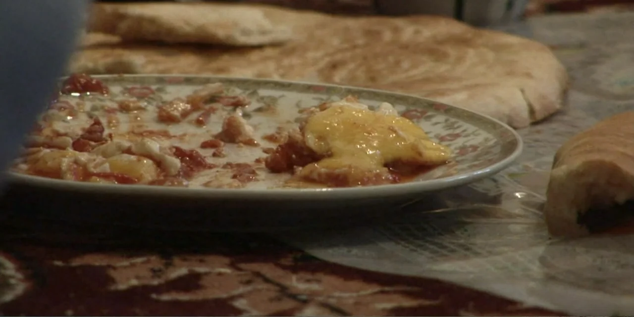 Silencing the Song: An Afghan Fallen Star (2011) movie still: closeup — A dinner table is set with a plate of cooked eggs in tomato sauce. Large…