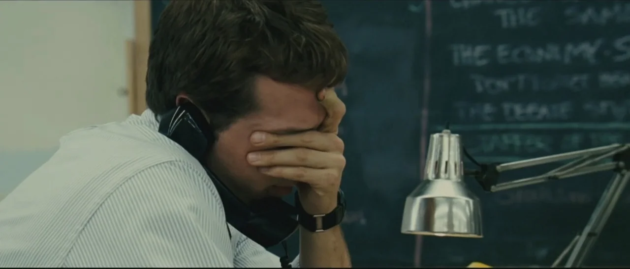 Definitely, Maybe (2008) movie still: closeup — A man sits at a desk in front of a dark chalkboard covered in writing. The subject holds a telephone…