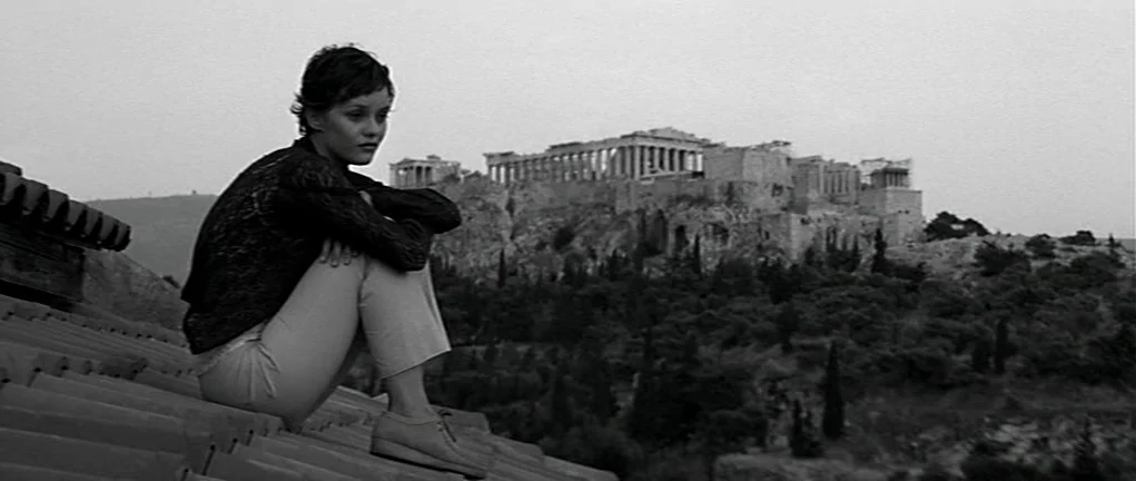 Girl on the Bridge (1999) movie still: fullbody — A woman sits on a terra cotta tiled roof overlooking an ancient stone monument. The Acropolis of…