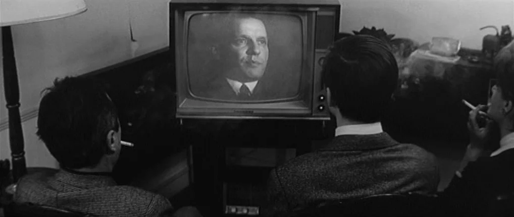 Antoine and Colette (1962) movie still: medium — Three people sit in a darkened room watching an old television set. A person's face is displayed…