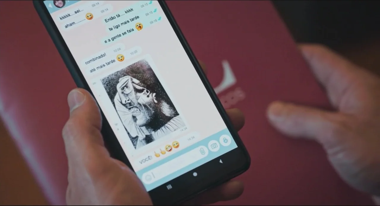 Proof of Love (2022) movie still: closeup — Hands hold a smartphone displaying an active messaging application interface. The screen shows a text…