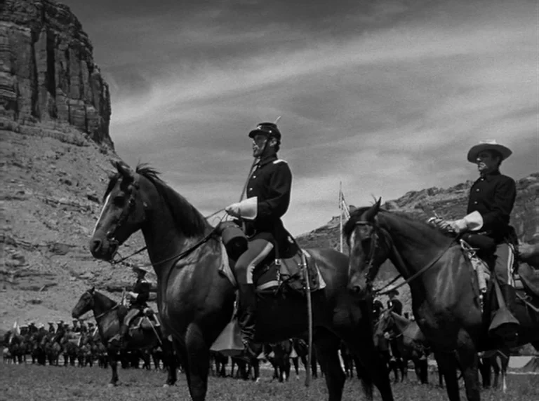 Rio Grande (1950) movie still: wide — A group of soldiers on horses gathers at the base of a large canyon. The men are wearing 19th-century military…