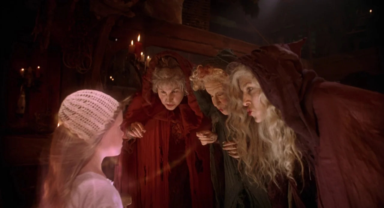 Hocus Pocus (1993) movie still: medium — Three cloaked women with expressive faces surround a young girl in a dimly lit room. The women stare…