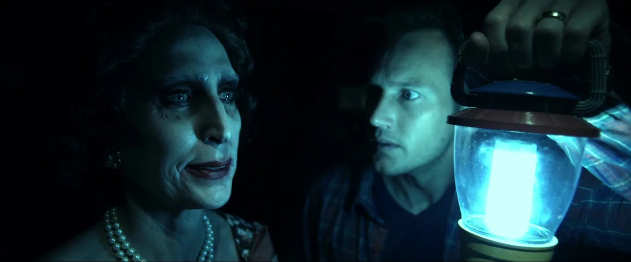 Insidious (2010) movie still: medium — A dark, windowless space illuminated only by a handheld electronic light source. A man shines a bright…