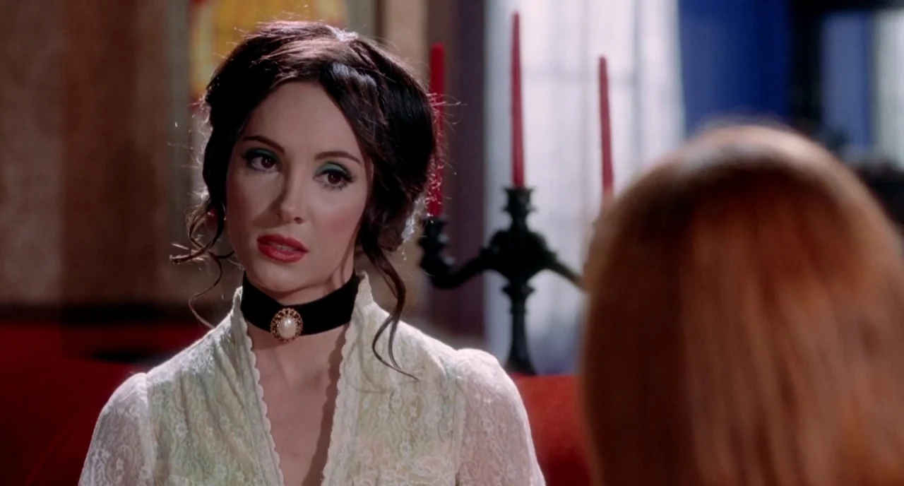 The Love Witch (2016) movie still: closeup — A dimly lit room features a woman sitting in front of a decorative candle holder. The woman gazes…