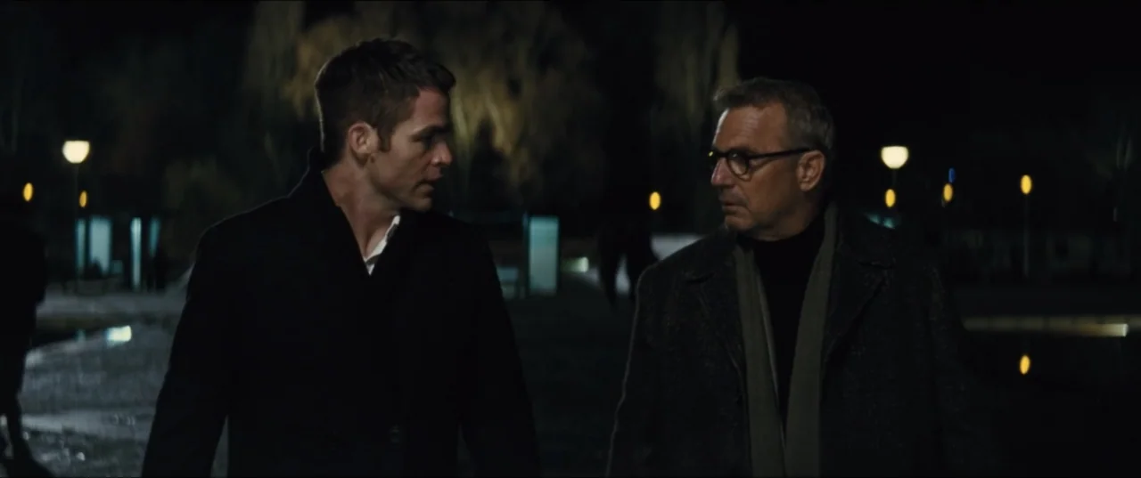 Jack Ryan: Shadow Recruit (2014) movie still: medium — A dark park at night features rows of glowing streetlamps in the distance. Two men in coats…