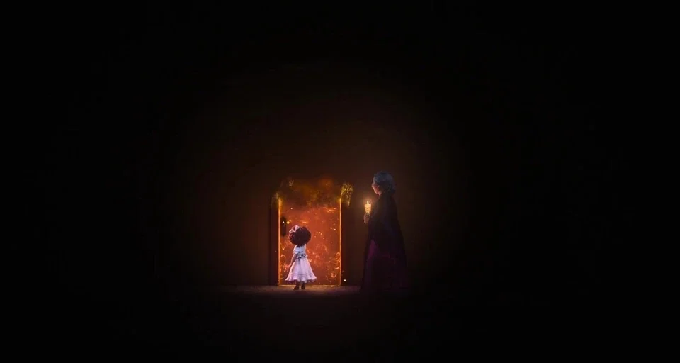 Encanto (2021) movie still: wide — A dark, expansive room surrounds a singular, brightly glowing doorway filled with embers. A young child faces the…