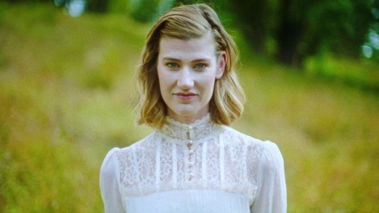 Strawberry Mansion (2021) movie still: medium — A woman stands in a blurred outdoor meadow filled with yellow-green grasses. She wears a vintage…