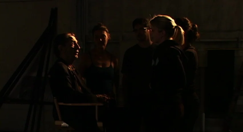 Inland Empire (2006) movie still: medium — An interior studio space is shrouded in deep shadow with minimal light exposure. A group of four people…