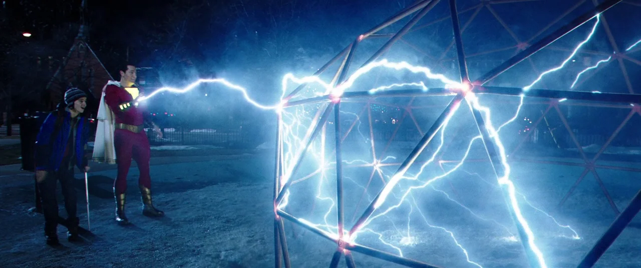 Shazam! (2019) movie still: wide — A snowy outdoor playground at night features a large, complex geometric metal frame. A man in a red superhero…