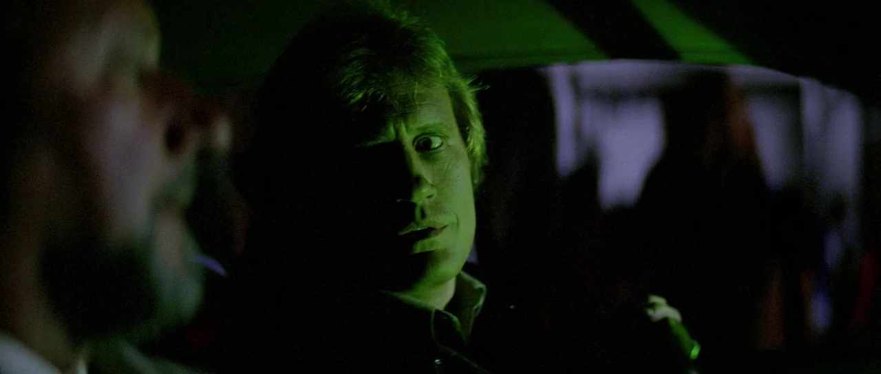 Halloween II (1981) movie still: medium — The interior of a car at night with dim, green-tinted lighting. A man stares toward a person sitting in…