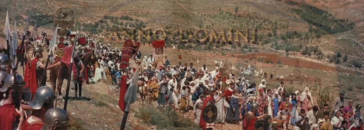 Ben-Hur (1959) movie still: wide — A vast crowd of people travels along a dusty path in a hilly landscape. Roman soldiers in traditional armor and…