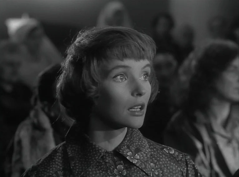 Head Against The Wall (1959) movie still: closeup — A crowded auditorium filled with blurred, out-of-focus figures seated in rows. A young woman in…