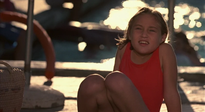Being John Malkovich (1999) movie still: medium — A poolside area at a beach or public pool with shimmering water in background. A young girl in a…