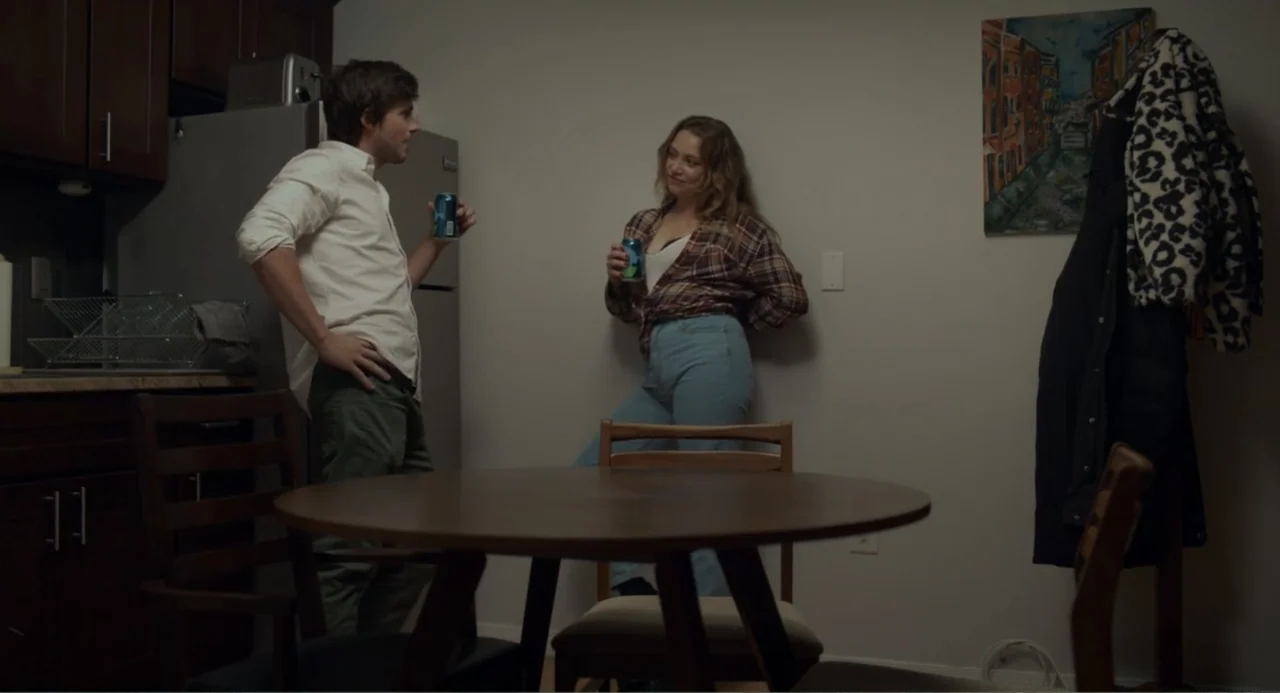This Closeness (2024) movie still: medium — A residential apartment with a wooden circular dining table and dark cabinetry. A young man and woman…