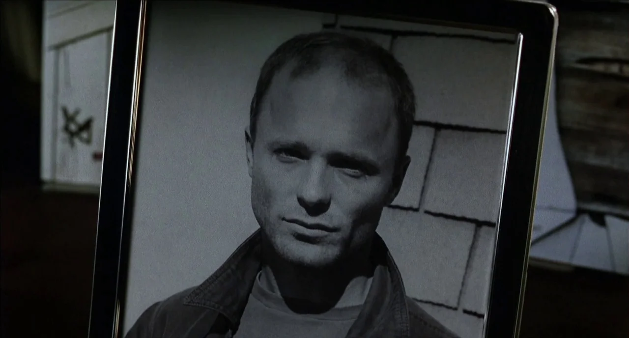The Hours (2002) movie still: closeup — A silver-framed photograph shows a man against a wall with shingle siding. The portrait is held or placed…