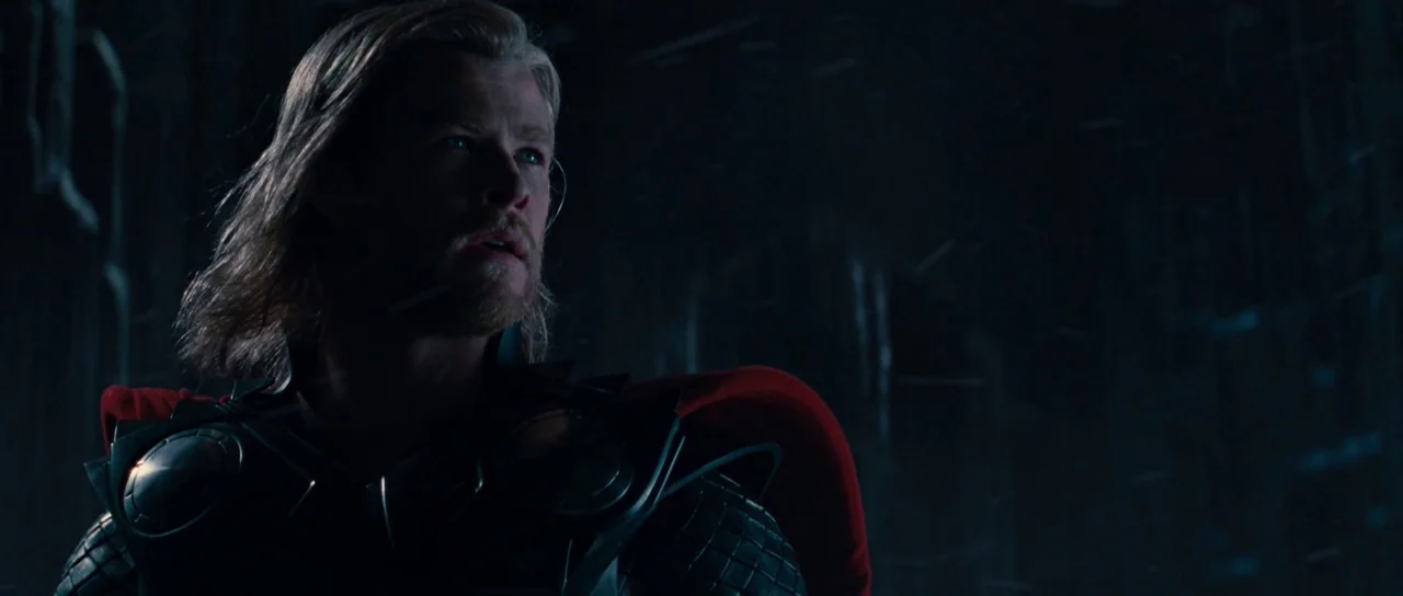 Thor (2011) movie still: medium — A dark, textured chamber with indistinct surfaces serves as a backdrop. A muscular man with blonde hair and…