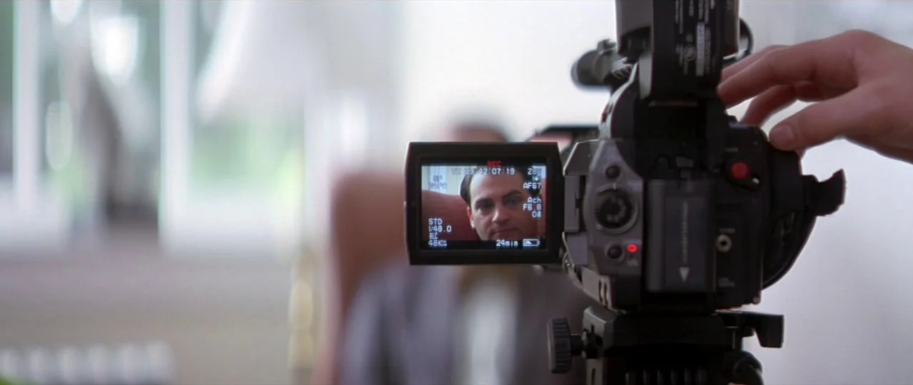 Afterschool (2008) movie still: medium — A bright living room features a person operating a professional camcorder on a tripod. The screen shows a…