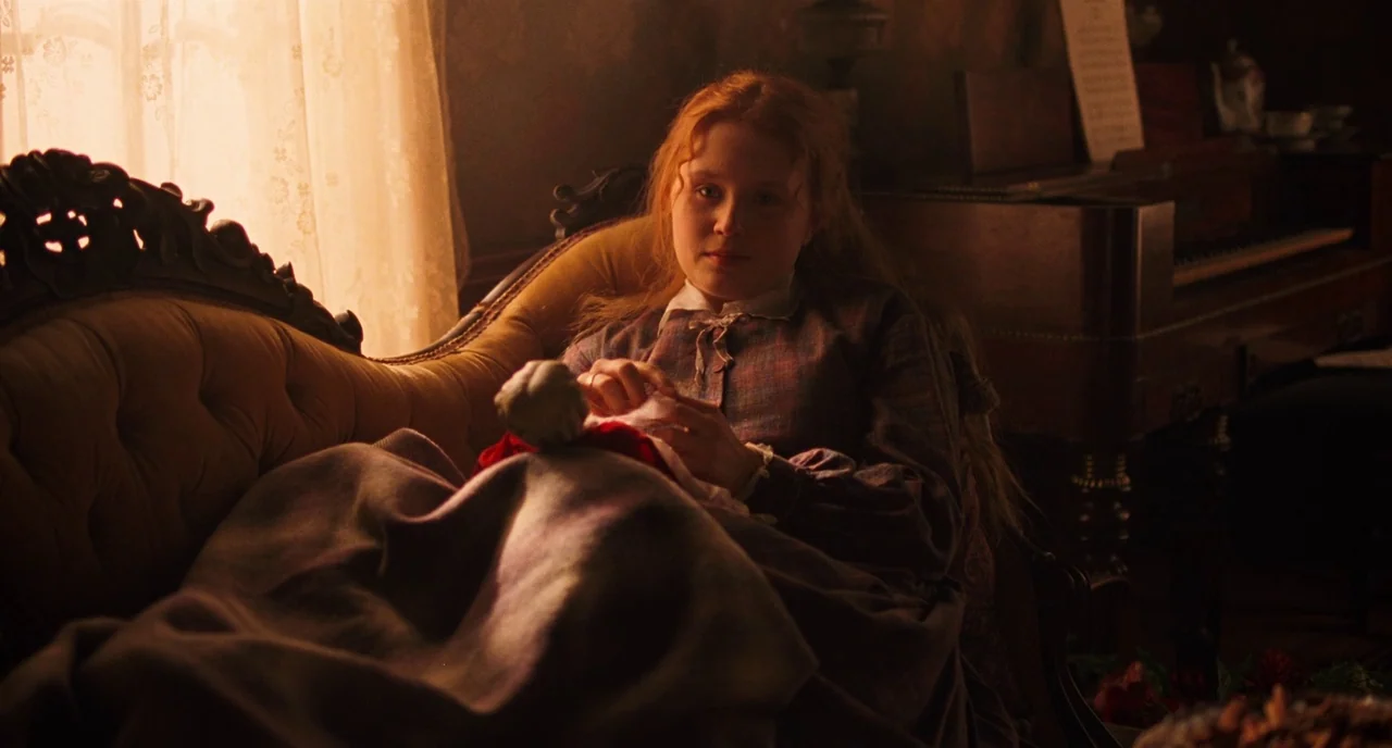 Little Women (2019) movie still: medium — A dimly lit 19th-century parlor features a velvet sofa and an antique piano. A young woman with auburn…
