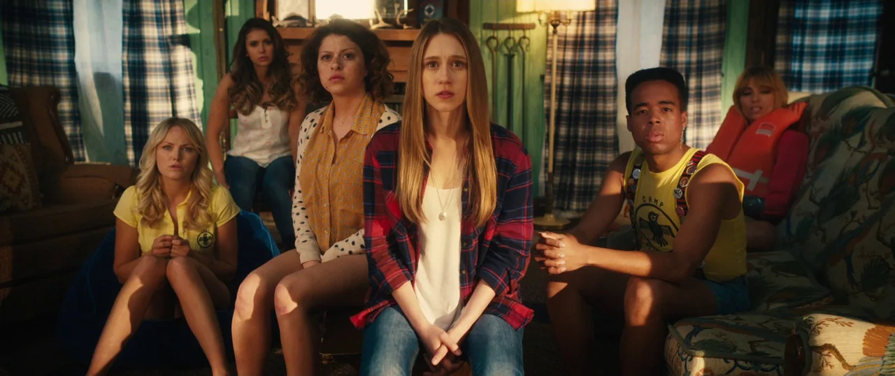Final Girls (2015) movie still: medium — A rustic wood-paneled room contains five young adults sitting on furniture looking ahead. The group…