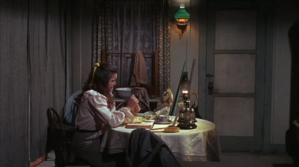 The Ballad of Cable Hogue (1970) movie still: medium — A dark dining area features a round table with a lace tablecloth and an oil lamp. A young…