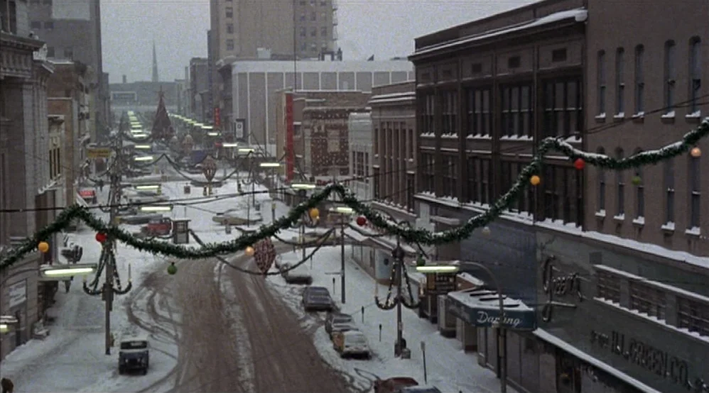 Hardcore (1979) movie still: establishing — A snow-covered downtown street features vintage 1940s storefronts and suspended holiday greenery…