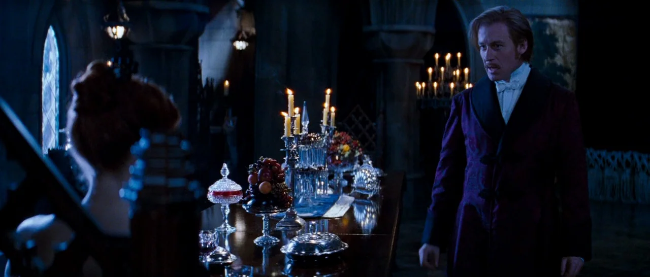 Moulin Rouge! (2001) movie still: medium — A dark stone dining hall features a long table filled with silver and fruit. A man in a velvet jacket…