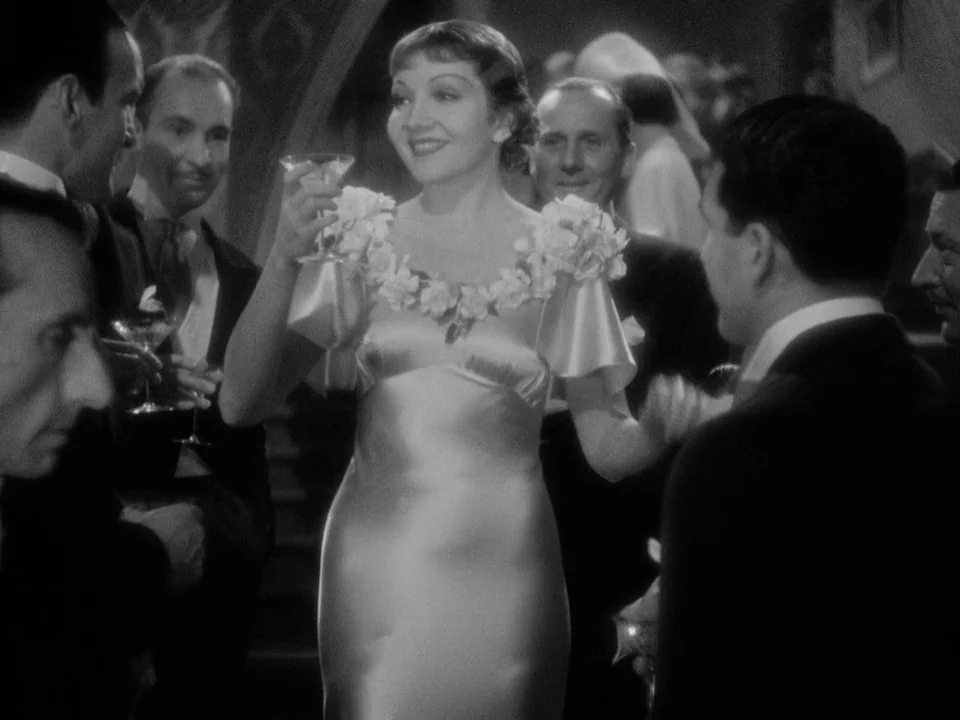 It Happened One Night (1934) movie still: medium — A crowded social event features men in dark formal suits surrounding a central woman. The woman…