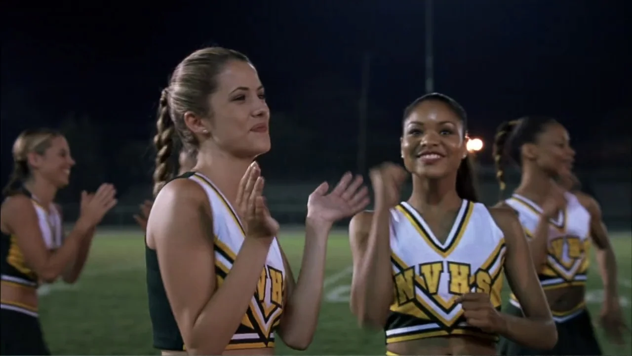 A Cinderella Story (2004) movie still: medium — A night view of a grass athletic field under bright stadium lighting. Three teenage cheerleaders in…