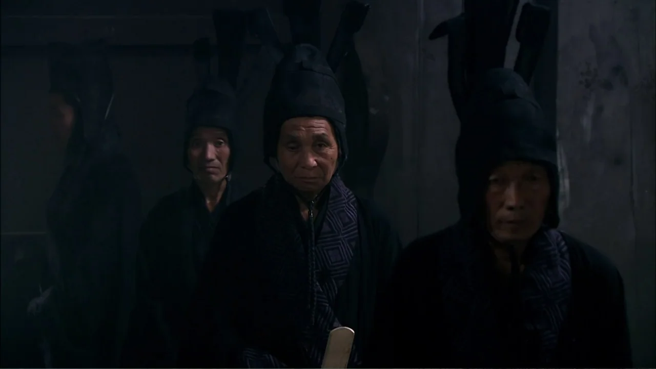 The First Emperor (2006) movie still: medium — A dark, sparsely lit interior space features stone-like walls and a stone floor. Three elderly men in…