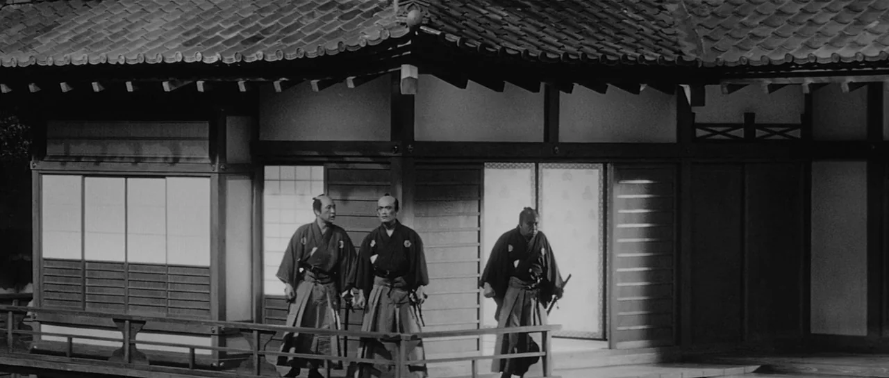 Sanjuro (1962) movie still: wide — A traditional wooden Japanese building exterior features paper shoji doors and a covered veranda. Three samurai…