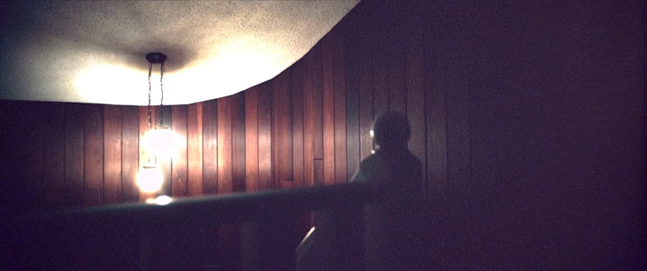Skinamarink (2022) movie still: medium — A dark stairwell features vertical wood-paneled walls and a rough-textured white ceiling. A silhouetted…