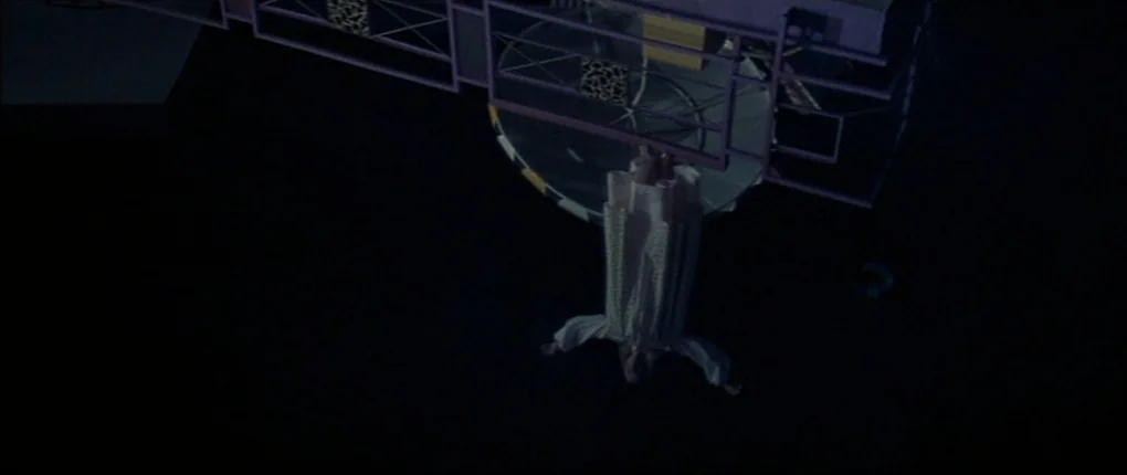 3 Women (1977) movie still: wide — An overhead shot of a dark outdoor platform structure with a geometric purple railing. A woman in a white dress…
