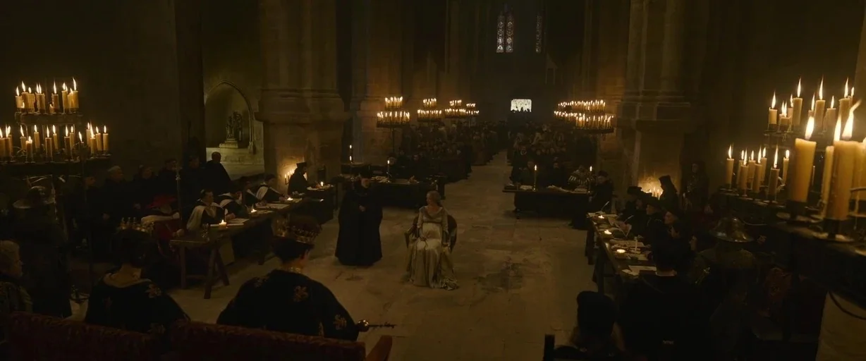 The Last Duel (2021) movie still: wide — A stone cathedral interior is crowded with people sitting at long wooden tables. A pregnant woman in a pale…