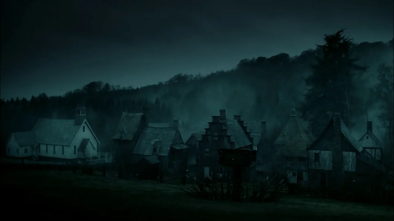 Sleepy Hollow (1999) movie still: establishing — A dark colonial village sits nestled at the edge of a dense, misty forest. The collection of wooden…