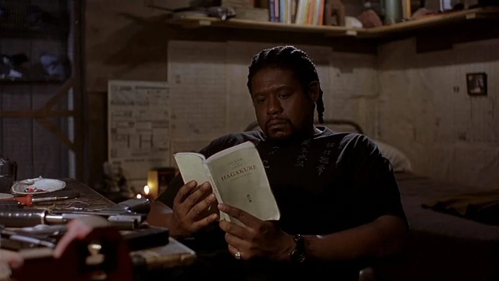 Ghost Dog: The Way of the Samurai (1999) movie still: medium — A dimly lit room with a workbench featuring organized tools and scattered papers. An…